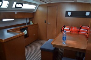 Eine kleine Küche mit Holdekor-Schränken, einer Arbeitsfläche und einer Bank. Auf dem Tisch steht eine Wasserflasche und an der Wand hängen orangefarbene Rettungswesten.