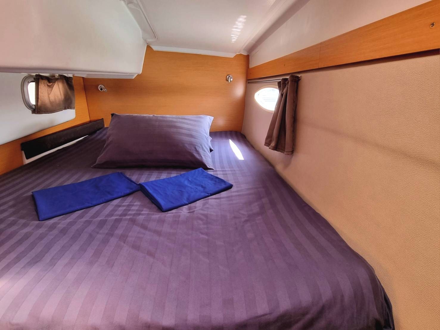 A compact bed with a headboard, a window with curtains, and a wall-mounted light fixture.