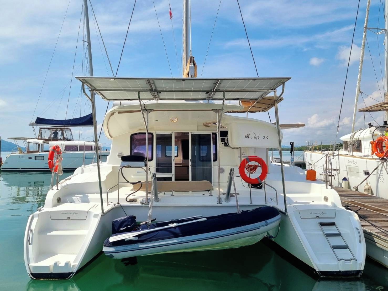 A white motorboat docked at a marina with a covered seating area, a lifebuoy, and a ladder.