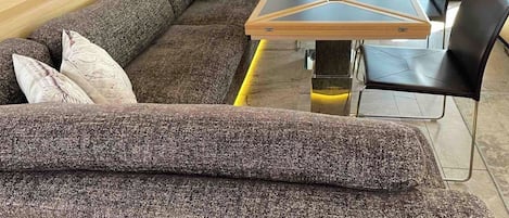Ein modernes Wohnzimmer mit einer Eckcouch, einem Glastisch und schwarzen Stühlen.