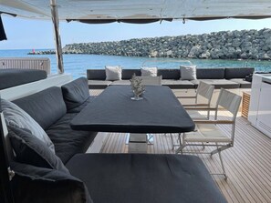 A covered outdoor seating area with a table and chairs, overlooking a rocky shoreline.