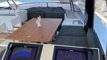 Le pont d’un yacht, avec une table en bois, des sièges rembourrés et deux écrans de navigation Simrad.