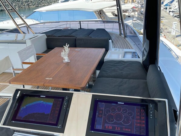 Le pont d’un yacht, avec une table en bois, des sièges rembourrés et deux écrans de navigation Simrad.