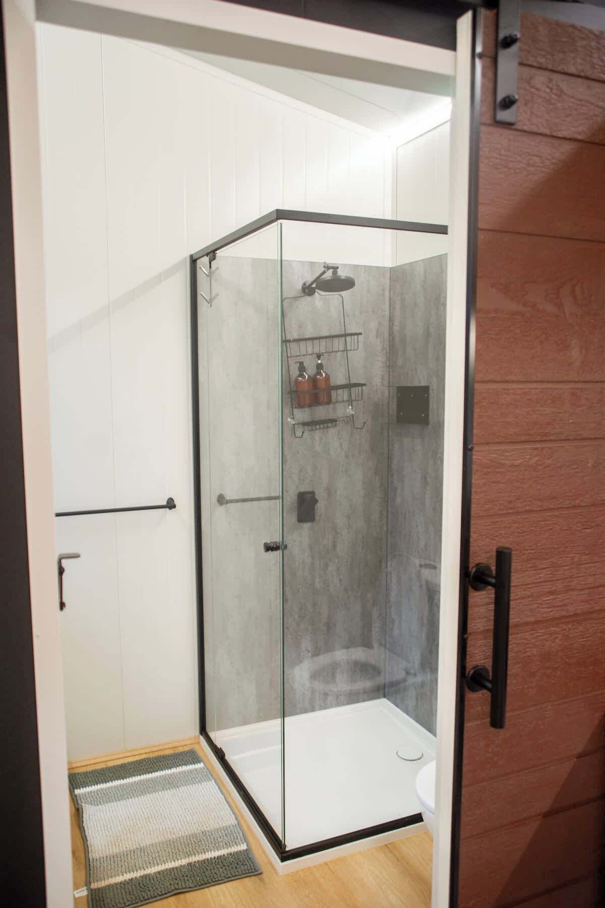 Une salle de douche fermée par des parois de verre, équipée d’une pomme de douche, d’un distributeur de savon et d’un porte-serviettes.