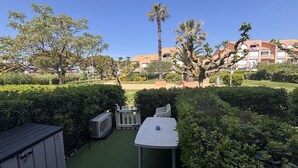 Une terrasse avec une table et des chaises, entourée de verdure et d’une clôture blanche.