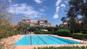 Une piscine rectangulaire à l’eau d’un bleu limpide, entourée d’une végétation luxuriante et bien entretenue, avec un bâtiment aux fenêtres en arc de cercle en arrière-plan.