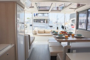 A boat interior with a dining area, seating, and a view of the outside.