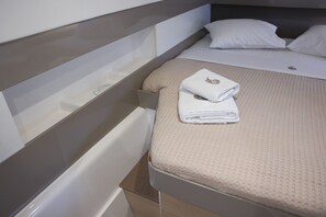 A neatly made bed with a folded towel, a headboard, and a bedside table.