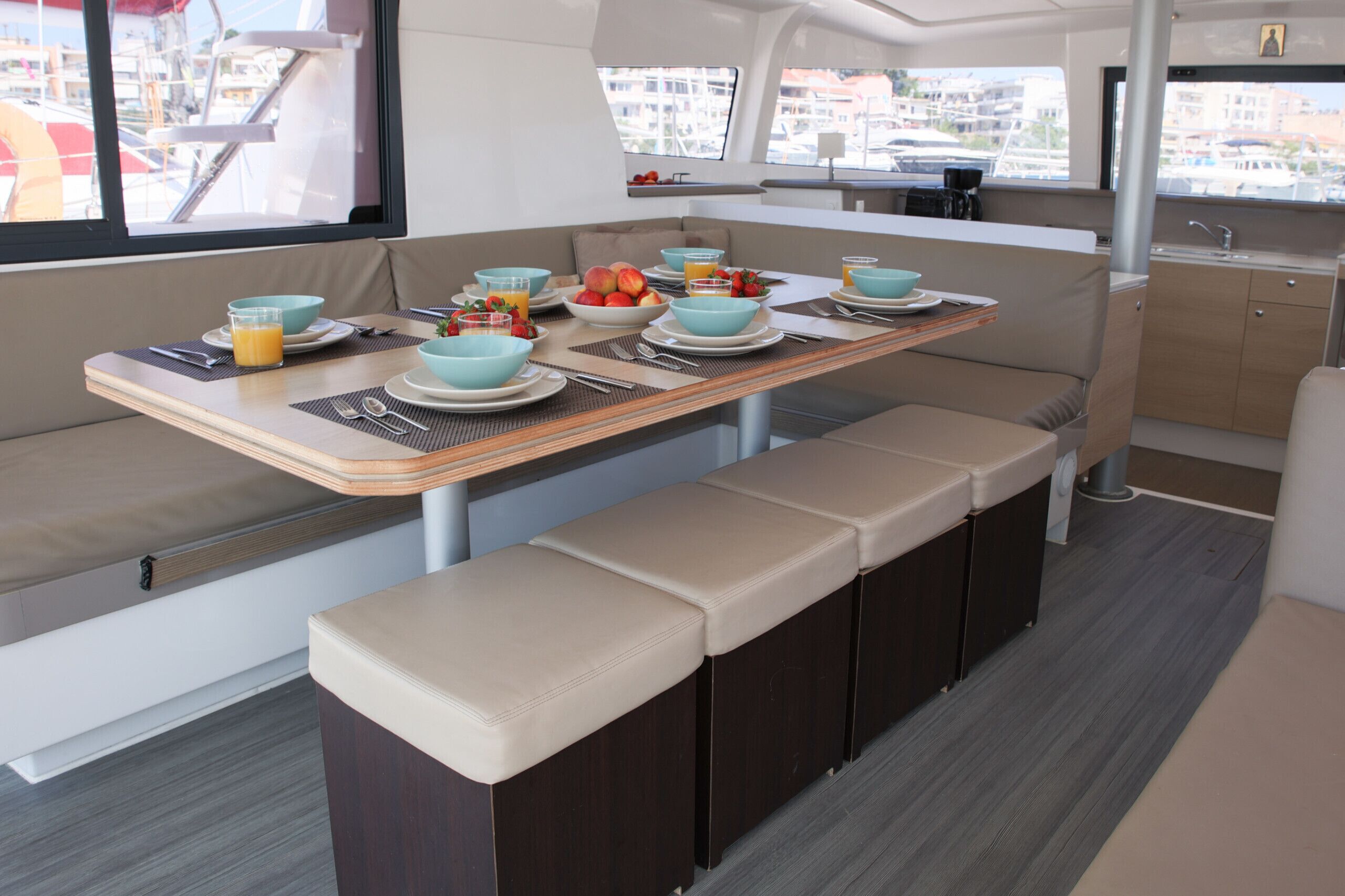 A compact galley with a dining table set for four, equipped with a sink and a window offering a view of the marina.