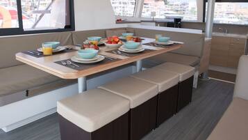 A compact galley with a dining table set for four, equipped with a sink and a window offering a view of the marina.