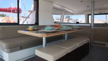 A boat interior with a dining area, seating, and a view of the marina.