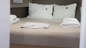 Ein ordentlich bezogenes Bett mit Kissen, einem gefalteten Handtuch und einem zusammengerollten Handtuch auf einer gemusterten Bettdecke.