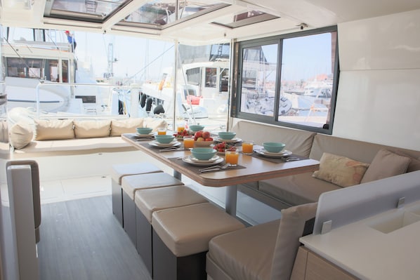 A boat's interior with a dining area, seating, and a view of the marina.