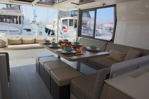 A dining area with a table set for breakfast, a view of the marina, and a seating area with cushions.