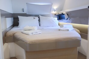 A modern, compact bedroom with a bed, pillows, a bedside table, and a small window. - Sun-kissed Sailing Adventure in the Ionian Islands (Preveza)