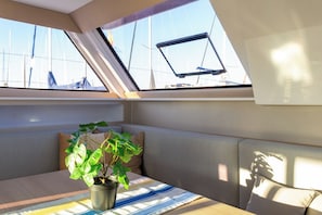 A cabin with a window overlooking sailboats, a cushioned bench, a potted plant, and a striped tablecloth. - Sun-Kissed Sailing: A Luxurious Beach Experience in Valencia (Denia)