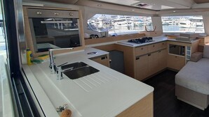 A compact galley kitchen with a sink, stove, and oven, and a view of the marina through large windows. - Sun-kissed Sailing Adventure in Split-Dalmatia, Croatia (Seget Donji)