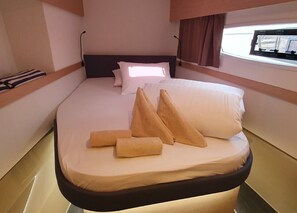 A bed with pillows and rolled towels, a headboard, and a window with curtains. - Sun-kissed Sailing Adventure in Split-Dalmatia, Croatia (Seget Donji)