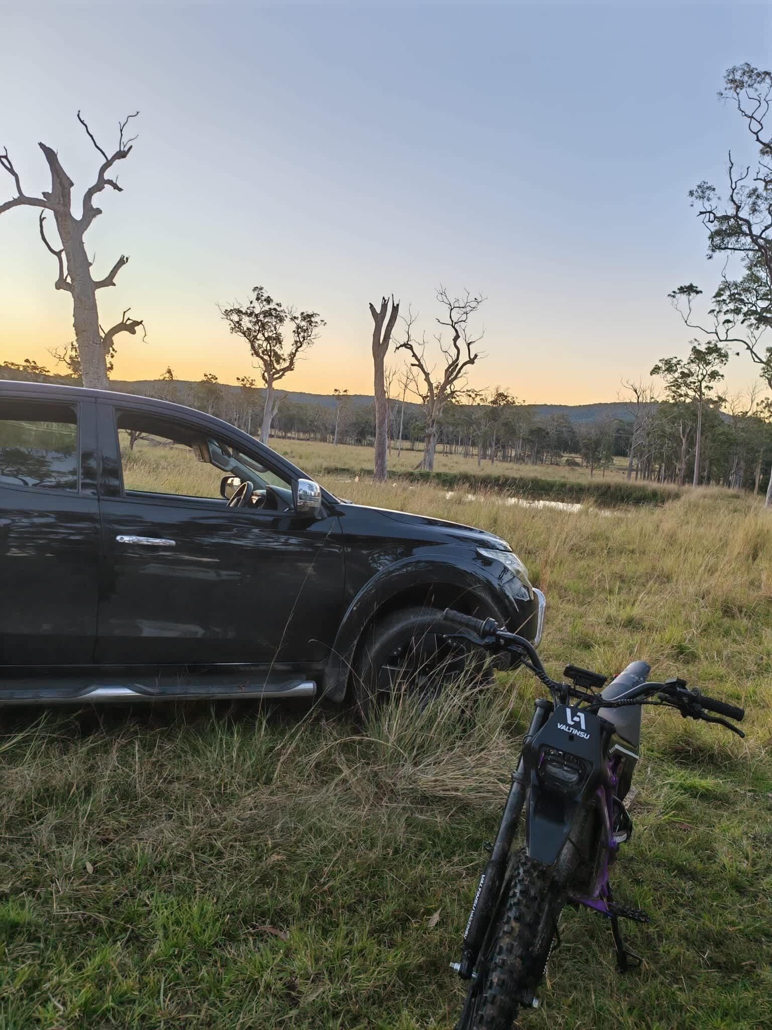 Een zwarte auto geparkeerd in een grasveld, met een berg en bomen op de achtergrond.