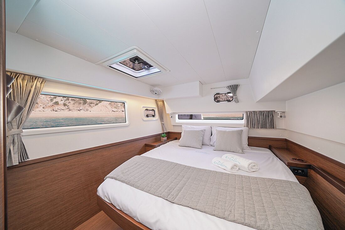 A modern bedroom with a large bed, a window with curtains, a small plant, and a ceiling light.