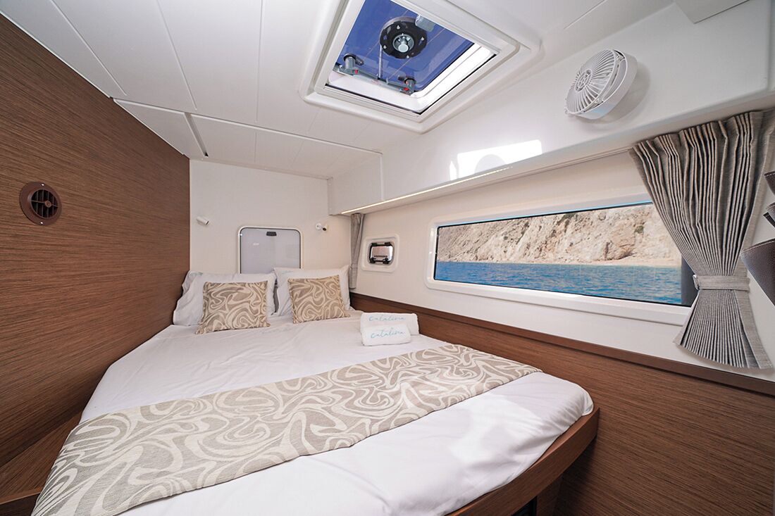 A bedroom with a bed, a skylight, a window with a view of the sea, and a fan.