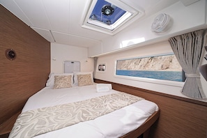 A bedroom with a bed, a skylight, a window with a view of the sea, and a fan. - Sun-kissed Sailing Adventure in the Ionian Islands (Preveza)