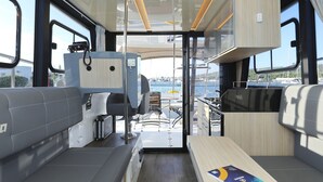 En modern inredning i en husbil med ett köksområde, sittplatser och utsikt över hamnen.