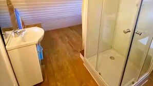 Ein Badezimmer mit Duschkabine aus Glas, Waschbecken und Holzboden.