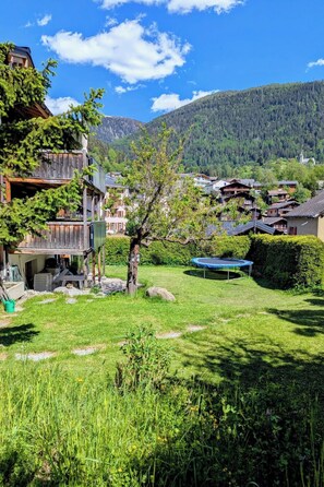 A rural village with traditional wooden houses, a clear blue sky, and a mountainous backdrop.