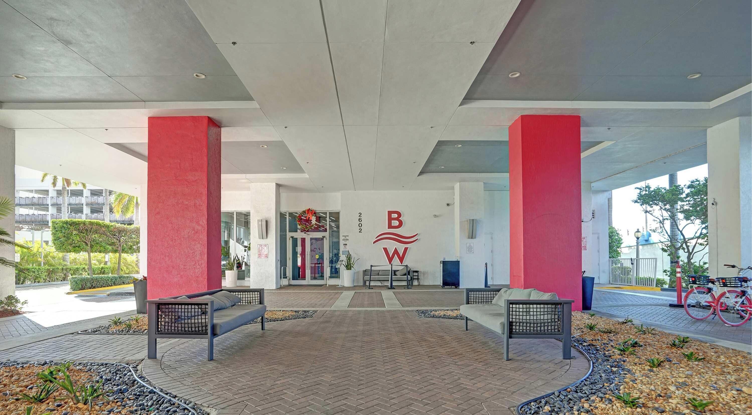 Un espace d’entrée abrité, agrémenté d’un logo rouge et blanc, de deux bancs et d’un chemin piétonnier dallé.