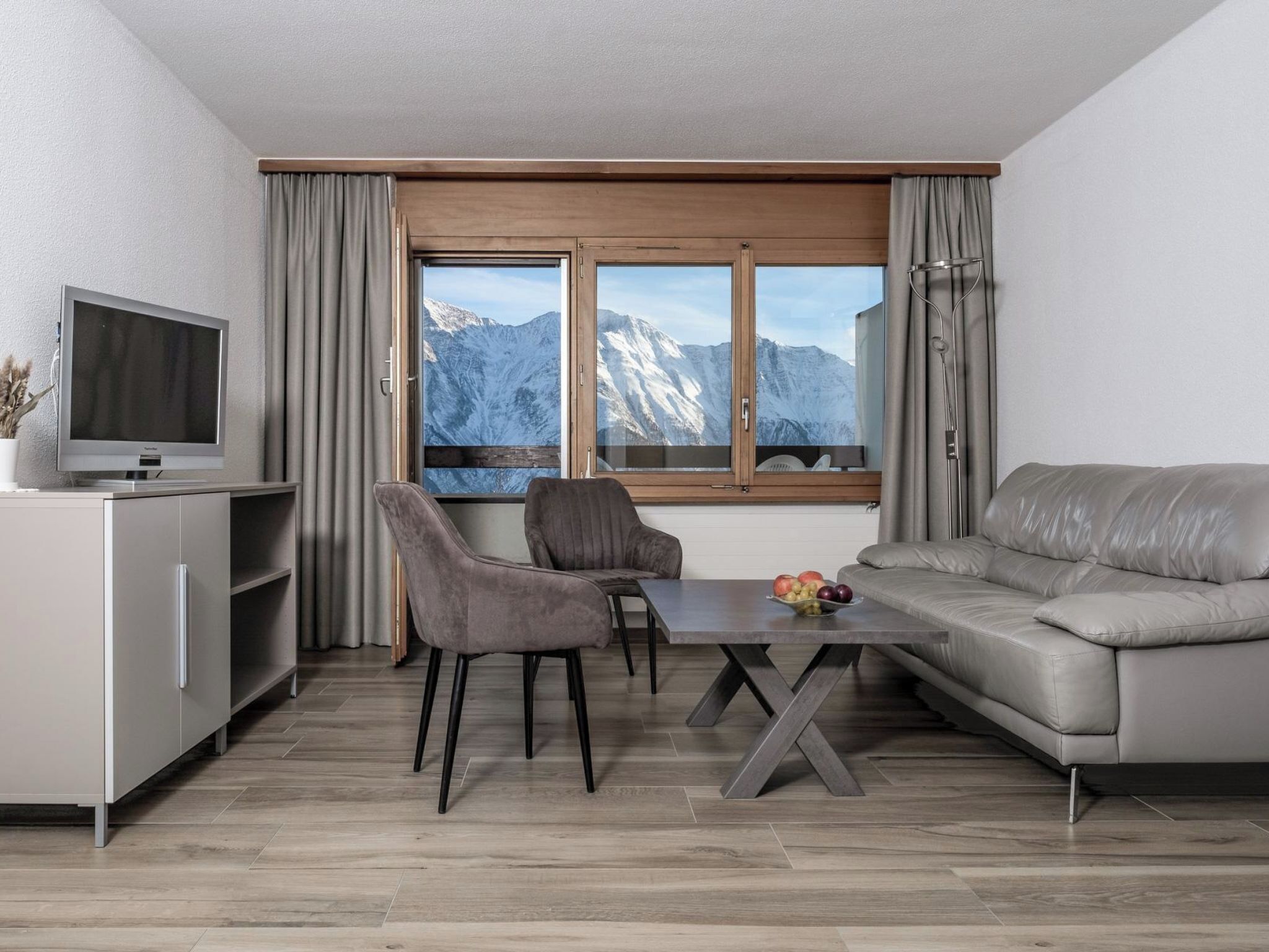 A modern living room with a sofa, two chairs, a dining table, and a TV.