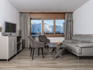 A modern living room with a sofa, two chairs, a dining table, and a TV.