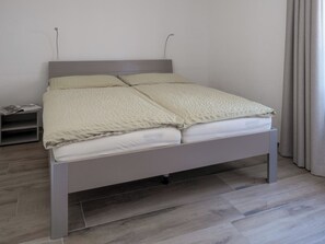 Een bed met grijs frame, wit beddengoed en een grijs hoofdeinde.