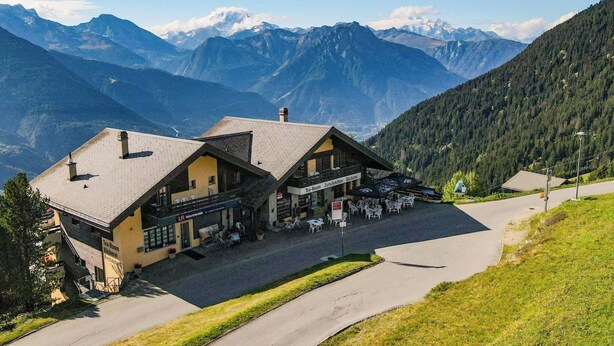 A mountain lodge with a restaurant, outdoor seating, and a view of the surrounding mountains.