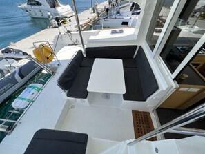 L'intérieur d'un bateau, avec un coin salon, une table et une vue sur le port de plaisance.