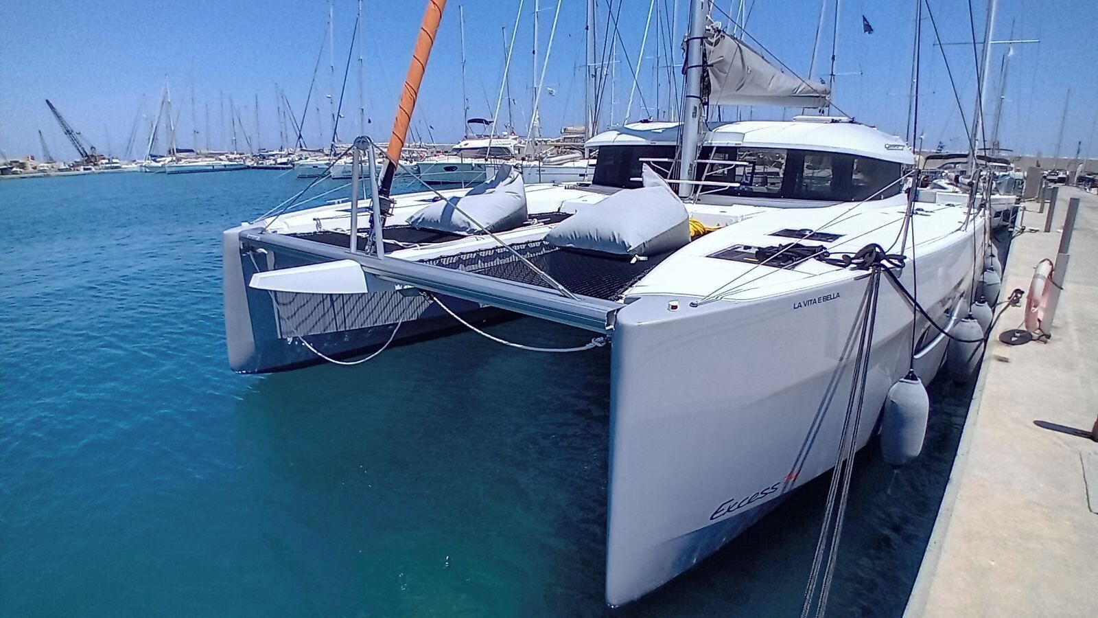 Ein weißes Katamaran liegt in einer Marina, im Hintergrund sind mehrere Segelboote zu sehen.