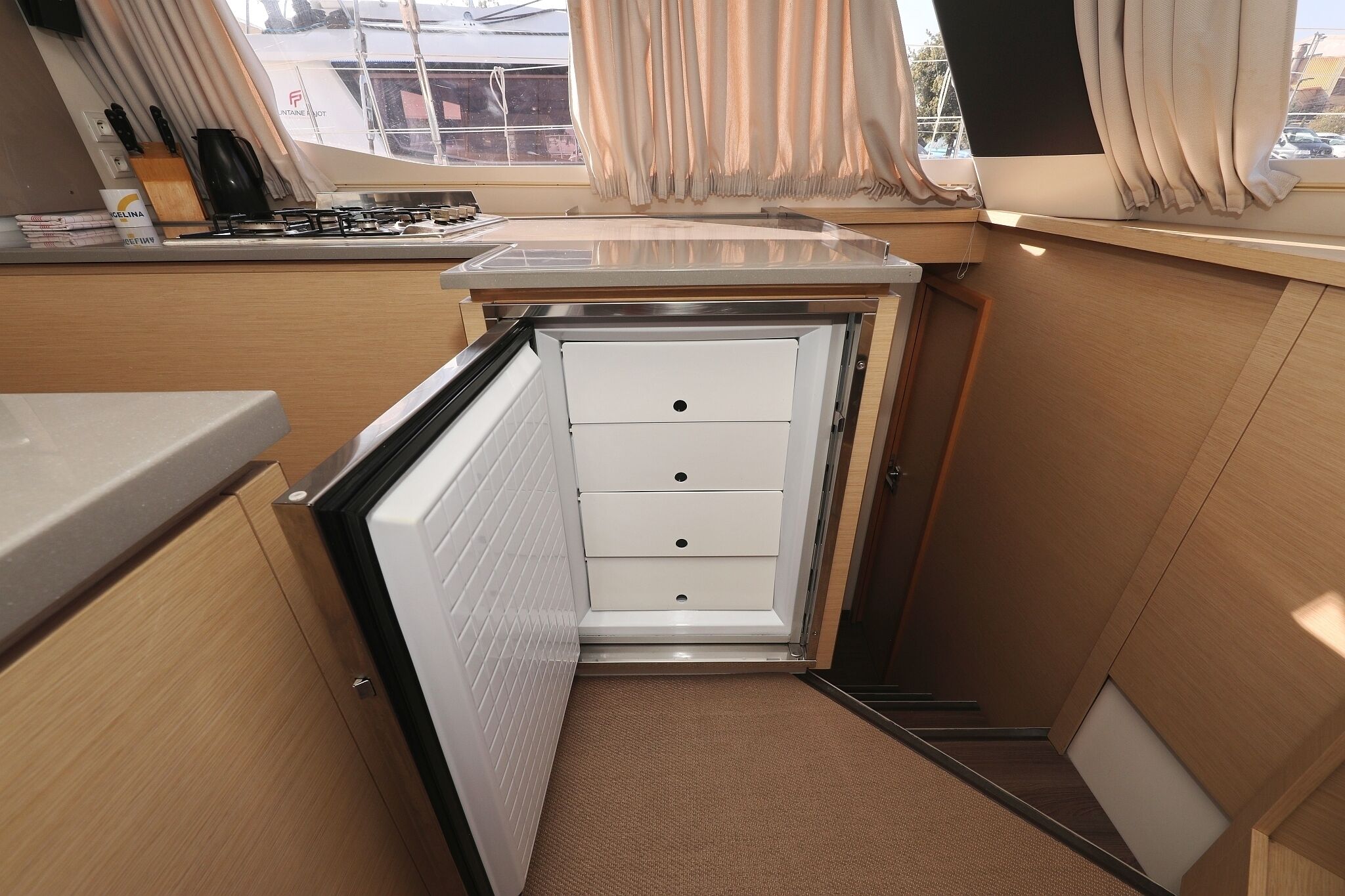 A compact kitchenette with a stove, a small countertop, and a window with curtains.