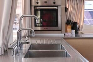 A modern kitchen with a stainless steel sink, a built-in oven, and a window with curtains. - Sun-kissed Sailing Adventure in Split-Dalmatia, Croatia (Trogir)