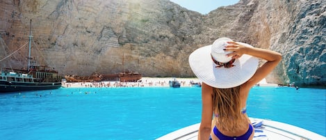 A person on a boat with a clear view of a rocky coastline and a beach.