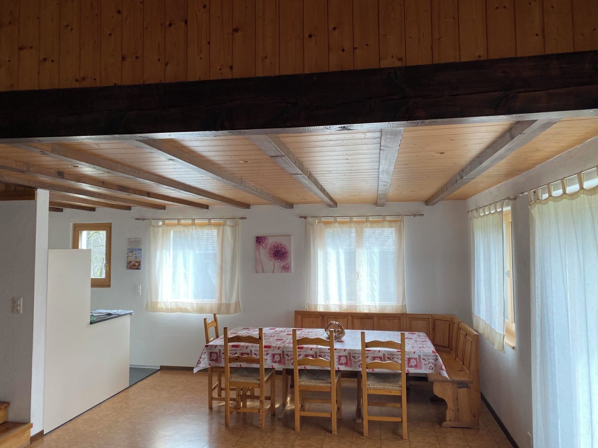 Un espace repas comprenant une table et des chaises en bois, un banc en bois, ainsi qu’un coin cuisine équipé d’un réfrigérateur.