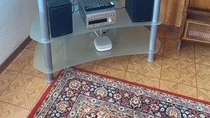 Ein Flachbildfernseher auf einem gläsernen TV-Möbel mit Fernbedienung, einer Stereoanlage und einem dekorativen Teppich.