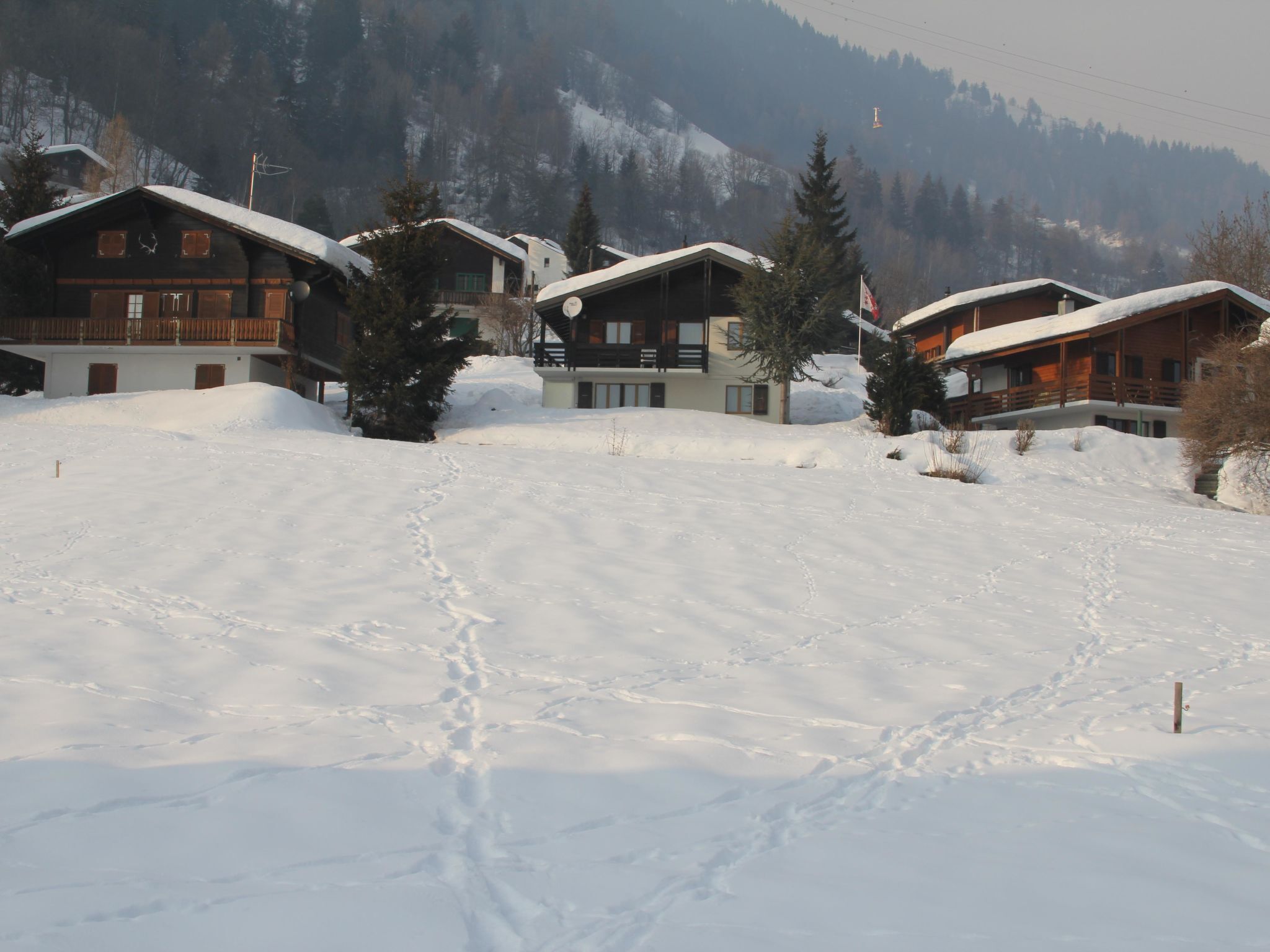 Un paysage enneigé avec des chalets en bois, un ciel dégagé et une montagne en arrière-plan.