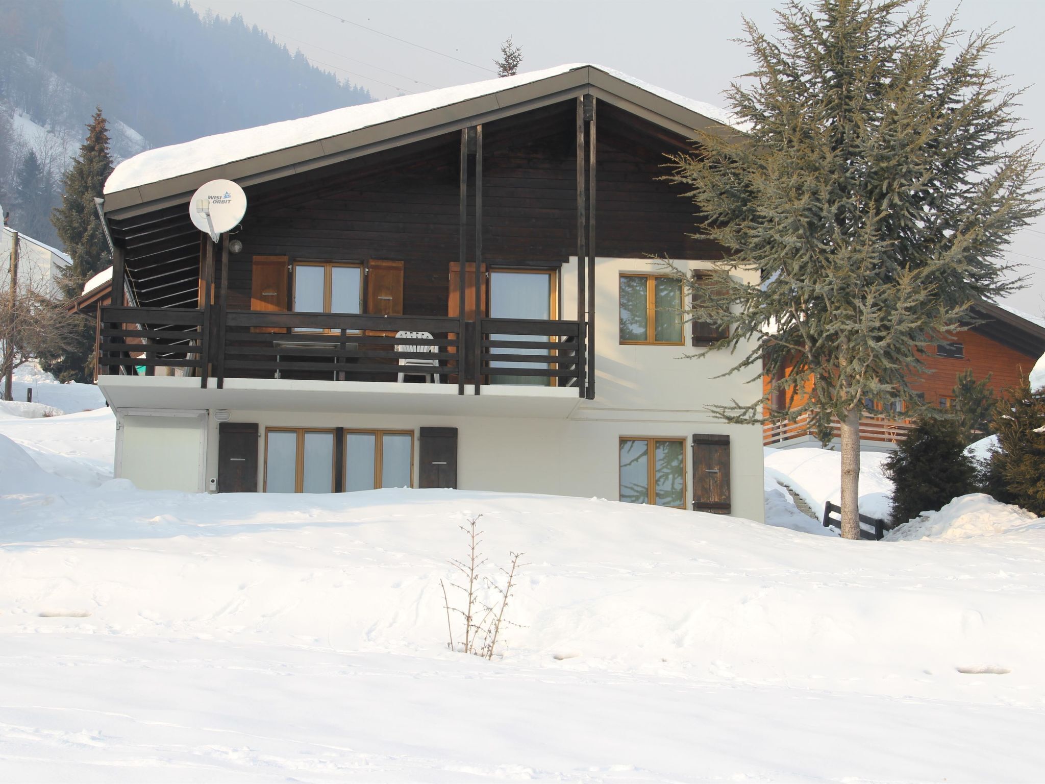 A wooden chalet with a balcony, a satellite dish, and a view of snow-covered mountains.