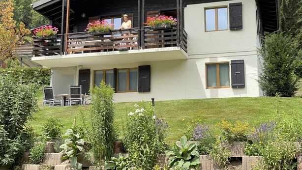 Ein zweistöckiges Gebäude mit einem Balkon, einem Essbereich mit Stühlen und einem Garten mit verschiedenen Pflanzen.