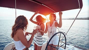 Un velero con toldo, gente sosteniendo bebidas y un mar tranquilo.