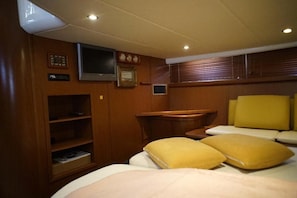 A cabin with a bed, a television, a small table, and a shelf with books.
