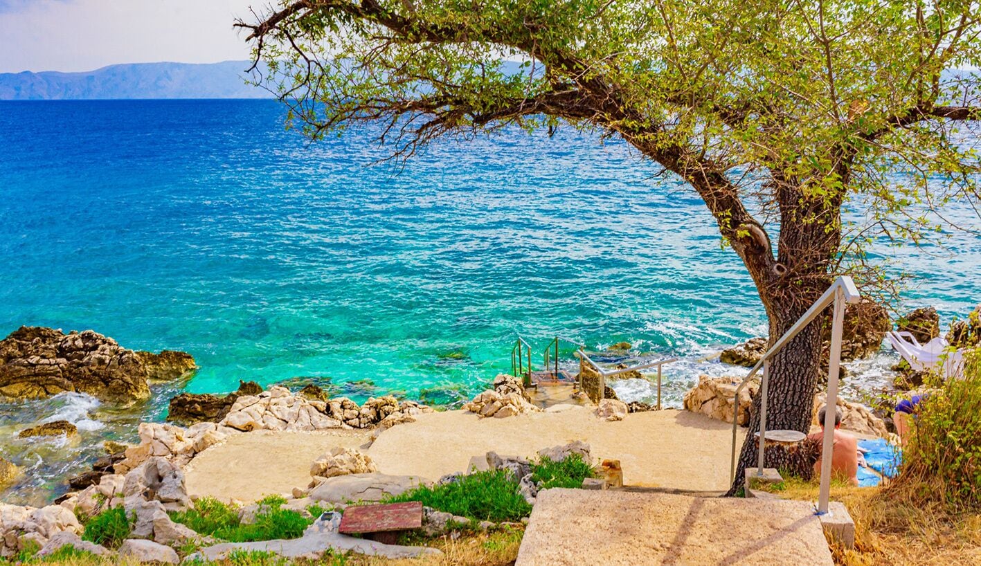 A coastal view with clear water, a tree, and a staircase leading to a beach.