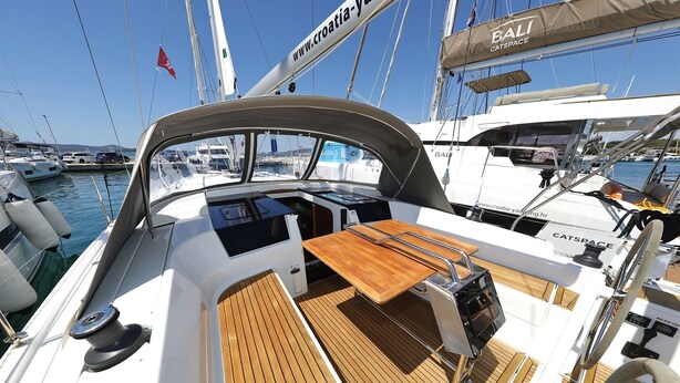Cubierta de barco con una mesa de madera, un timón y un catamarán llamado 'BALI' al fondo.