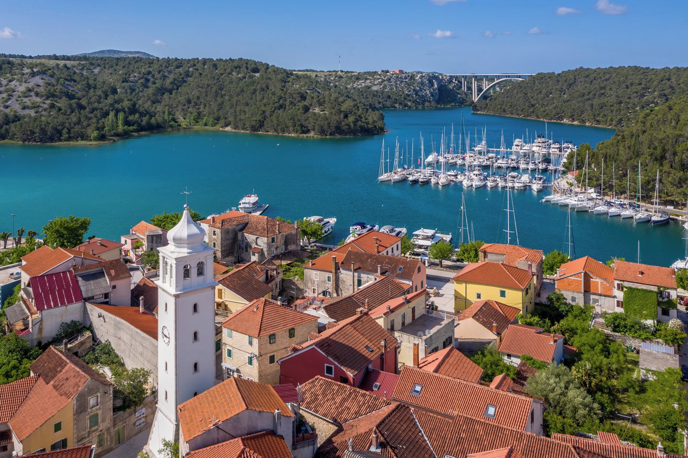 Une ville côtière dotée d’un port de plaisance, de bâtiments aux toits rouges et d’une église blanche imposante.