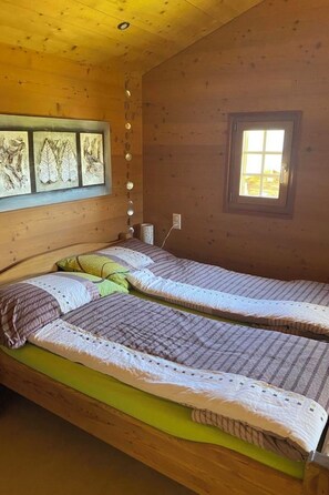 A wooden cabin room with two beds, a window, and wall-mounted lights. - Alphütte Bielerhüs Appartement/Fewo, Dusche, WC 3 Zimmerwohnung, 4-Betten by Interhome (Fiesch)